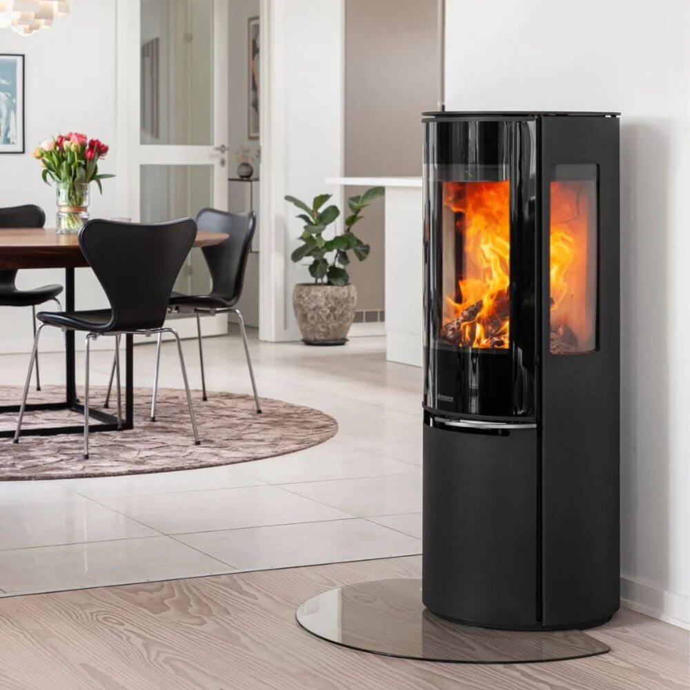 Elegant Aduro 22.5 Lux braskamin med helglas och sidoglas placerad på glasskiva i ett ljust hem
