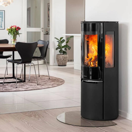 Elegant Aduro 22.5 Lux braskamin med helglas och sidoglas placerad på glasskiva i ett ljust hem