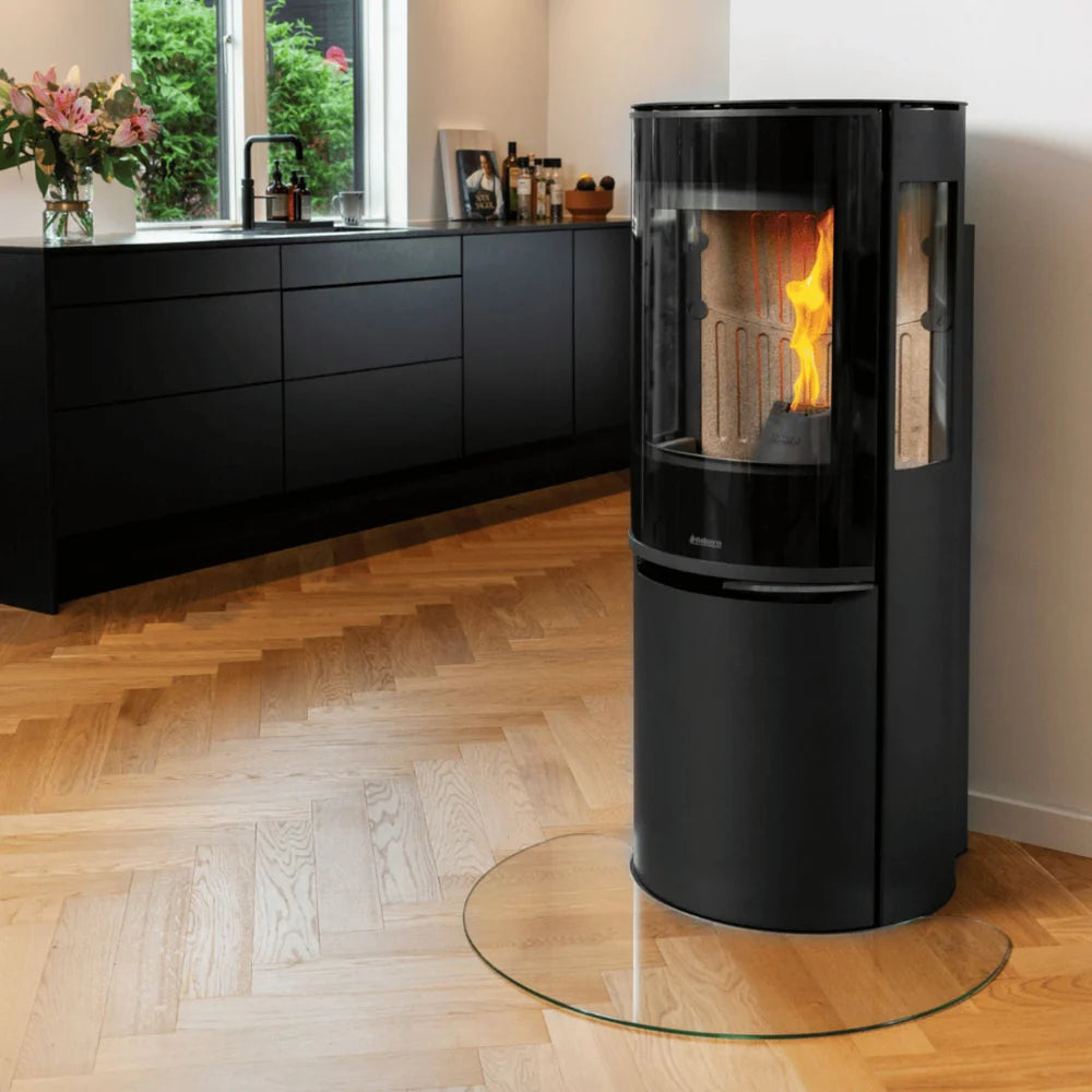 Svart Aduro P5 Lux pelletskamin monterad på glasskiva i ett stilrent kök med trägolv