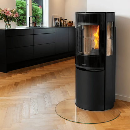 Svart Aduro P5 Lux pelletskamin monterad på glasskiva i ett stilrent kök med trägolv
